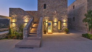 A stone building with a staircase leading to a door, surrounded by plants and a view of the landscape. - Villa Helia With Swimming Pool (Paros)
