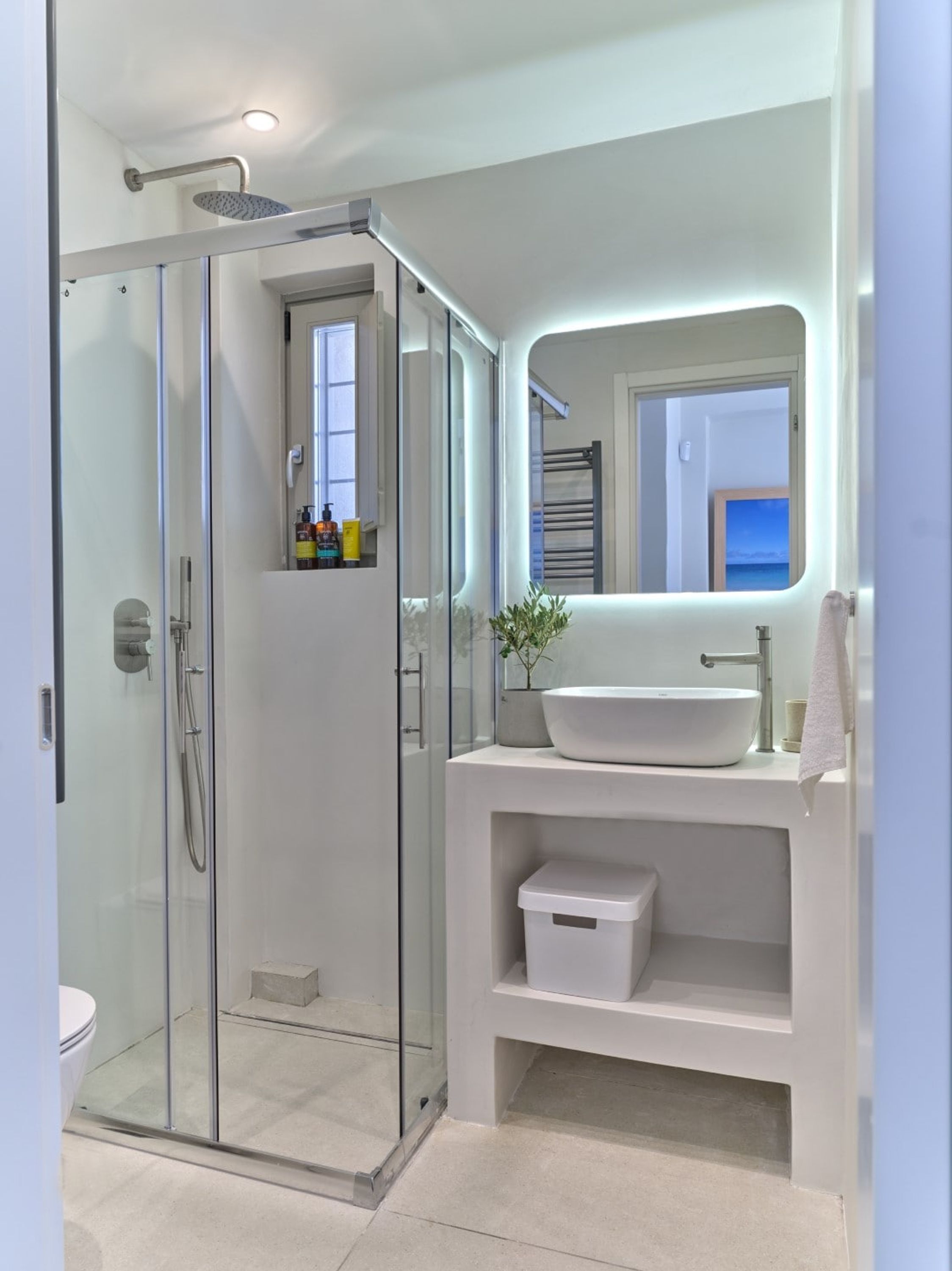 Un bagno moderno con doccia vetro, lavabo bianco e specchio vista mare.