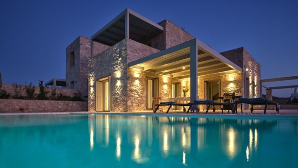 A modern building with a pool, stone facade, and outdoor seating area. - Villa Helia With Swimming Pool (Paros)