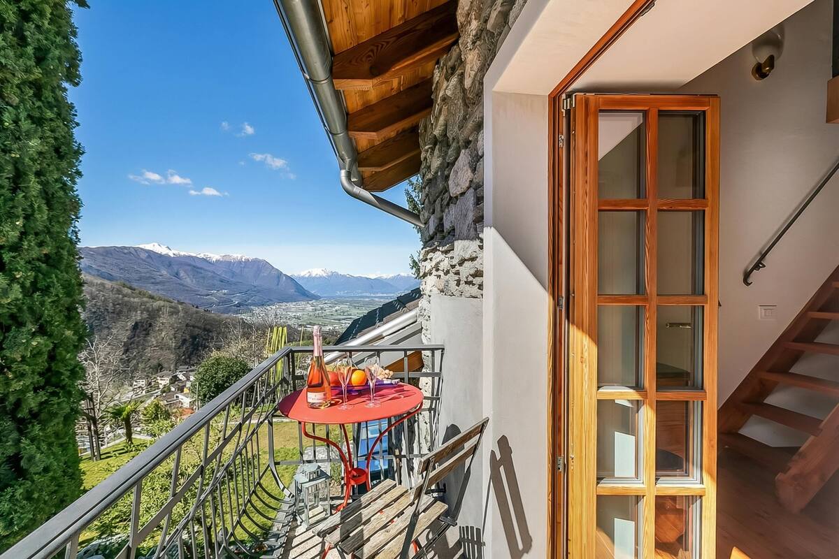 Ein Balkon mit Tisch, Flasche und Gläsern, mit Blick auf eine gebirgige Landschaft.