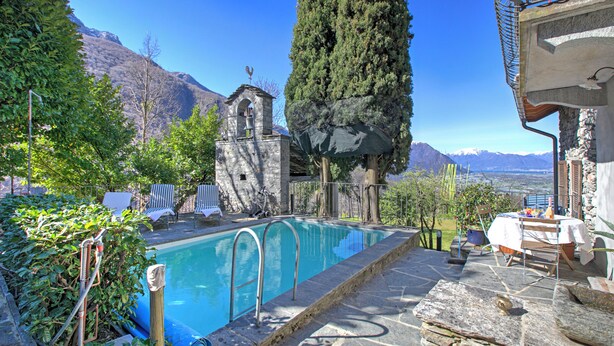 Una piscina amb escales de pedra, envoltada de vegetació i una torre de campanar.