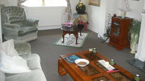 A living room with a grey armchair, a wooden coffee table with a bowl and books, a small side table with a vase, and a cabinet with decorative items. - Room-large Home in Prime Location for al (Wetherby)