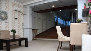 A modern lobby with a staircase, a sofa, a coffee table, and a vase with flowers. - Hotel Carmen Galaxi (Malabo)
