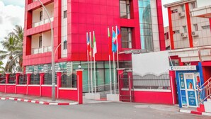 A multi-story building with a red facade and a glass elevator shaft. - Hotel Carmen Galaxi (Malabo)