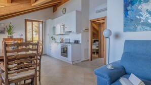 A modern kitchen with white cabinets, a dining area with a wooden chair, and a blue sofa with a book. - Il Nido sul Lago by Varenna Holidays (Perledo)
