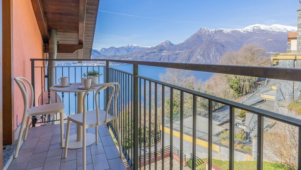 A balcony with a table and chairs, overlooking a mountainous landscape and a body of water. - Il Nido sul Lago by Varenna Holidays (Perledo)