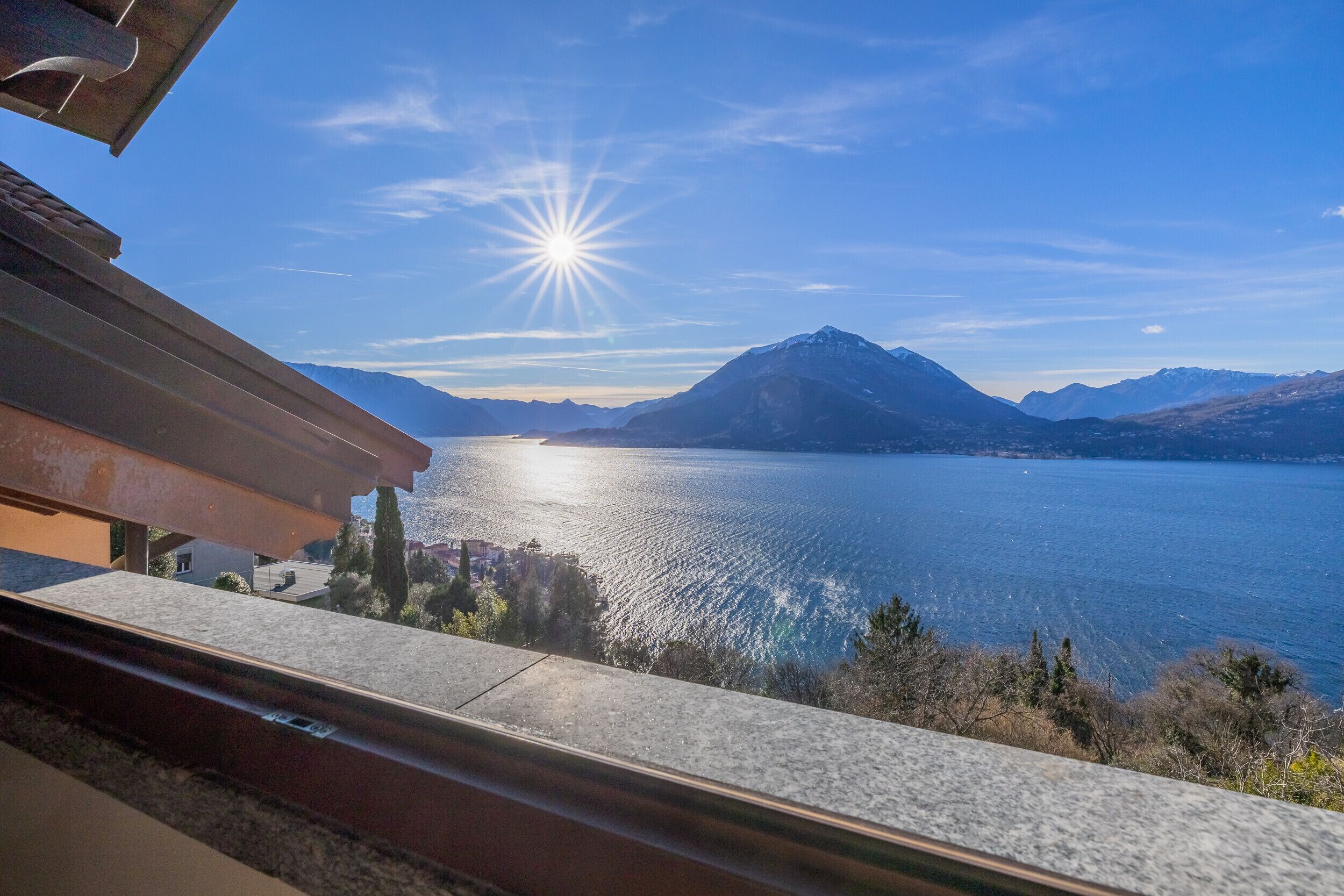 Vista desde un balcón sobre un lago, con montañas al fondo.
