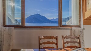 A room with a large window offering a mountain view, wooden chairs, and a table. - Il Nido sul Lago by Varenna Holidays (Perledo)