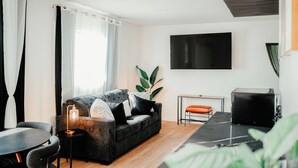 Een moderne woonkamer met een bank, een eettafel en een aan de muur bevestigde televisie.