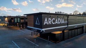 Een modern hotel genaamd 'Arcadia Hotel' met een opvallend bord, een overdekte parkeerplaats en uitzicht op de lucht.