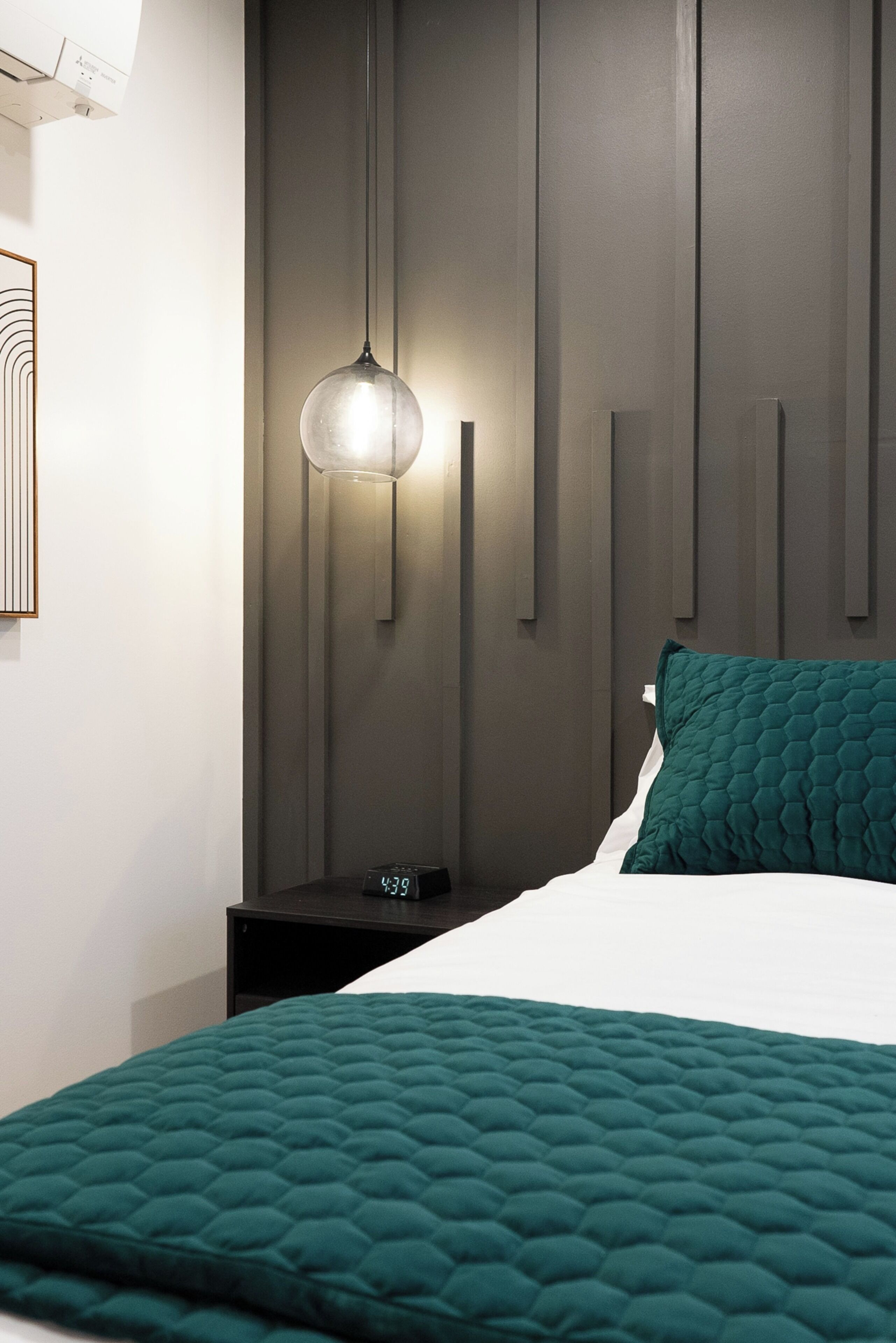 A modern bedroom with a bed, a bedside table with a clock, and a wall-mounted light fixture.