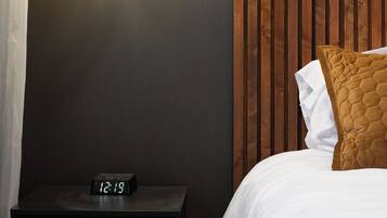 A bedroom with a bed, a nightstand with a digital clock, a hanging light fixture, and a wooden panel wall.