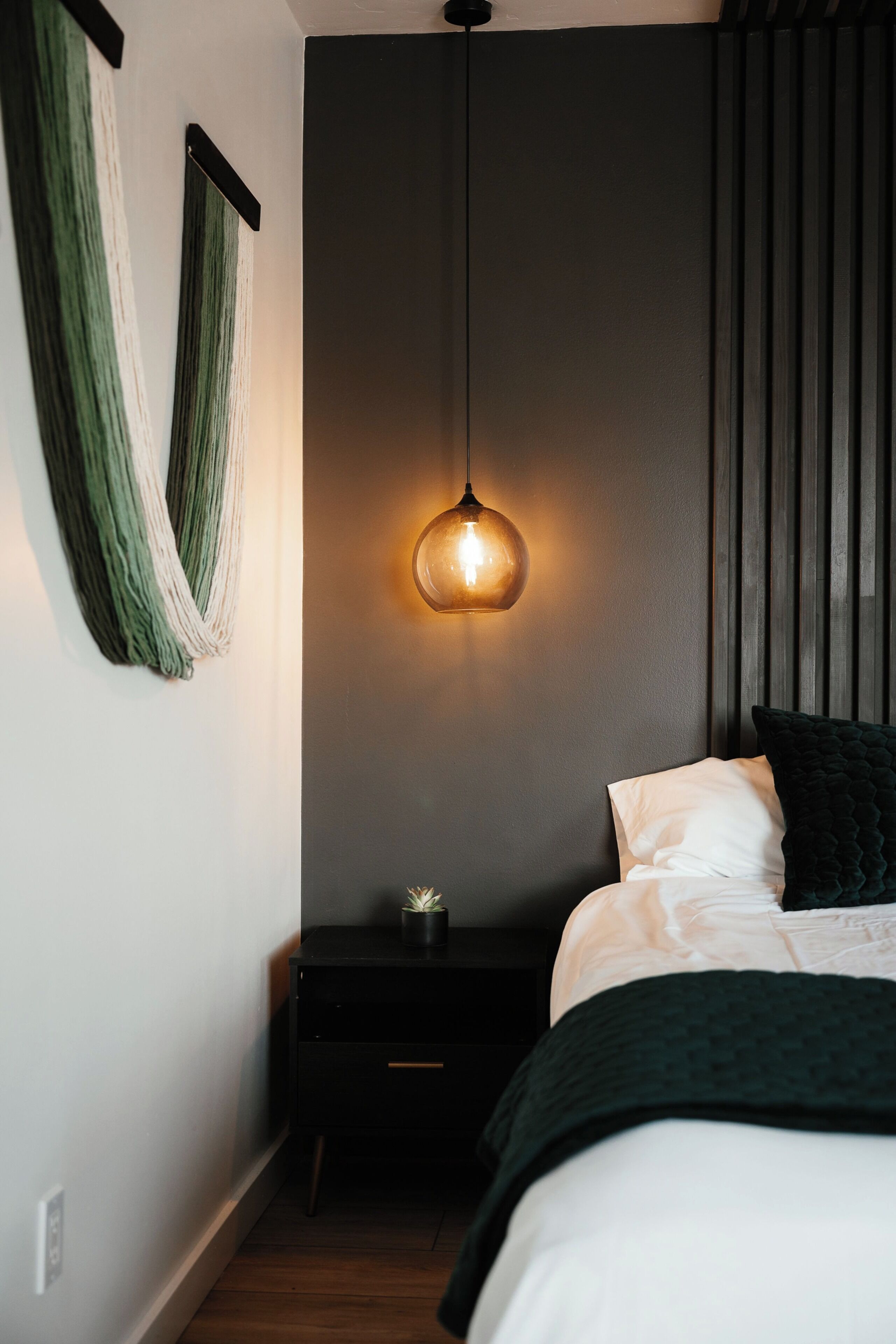 A bedroom with a bed, a bedside table, a hanging light fixture, and a wall-mounted curtain.