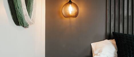 A bedroom with a bed, a bedside table, a hanging light fixture, and a wall-mounted curtain.