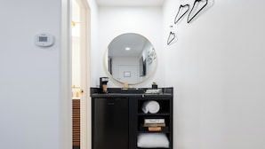 Een compacte badkamer met een zwart aanrecht, een ronde spiegel en een klein plankje met boeken en handdoeken.