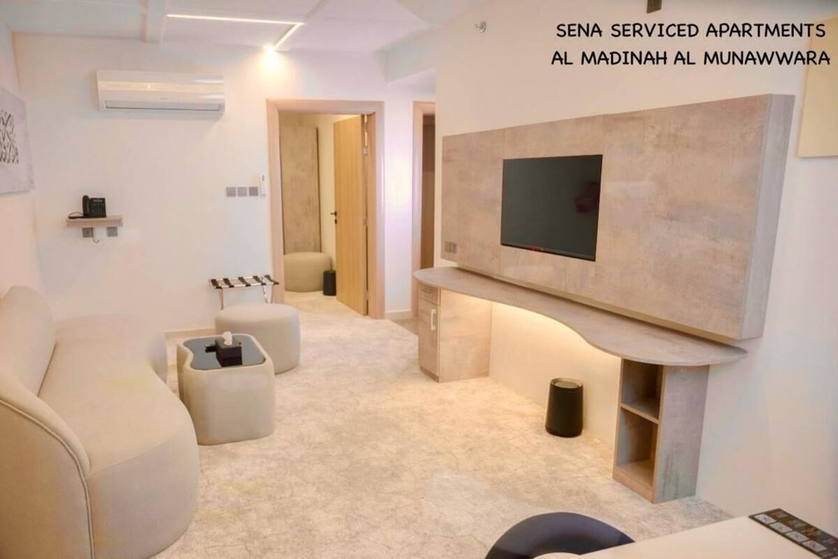 Un salon moderne avec un canapé, un pouf et un téléviseur à écran plat fixé au mur.
