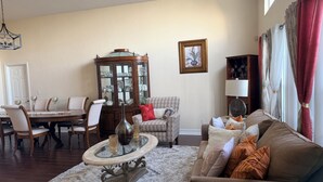 Un salon comprenant une table à manger, des chaises, une table basse avec un plateau en verre, un fauteuil à motifs, un canapé et un meuble avec des portes en verre.