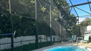 Une piscine d’un bleu éclatant, équipée d’une échelle de sécurité, entourée d’une clôture blanche et d’arbres.