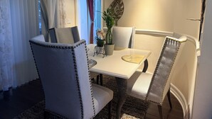 Un coin repas comprenant une table blanche, quatre chaises rembourrées, une plante en pot et un élément décoratif mural.