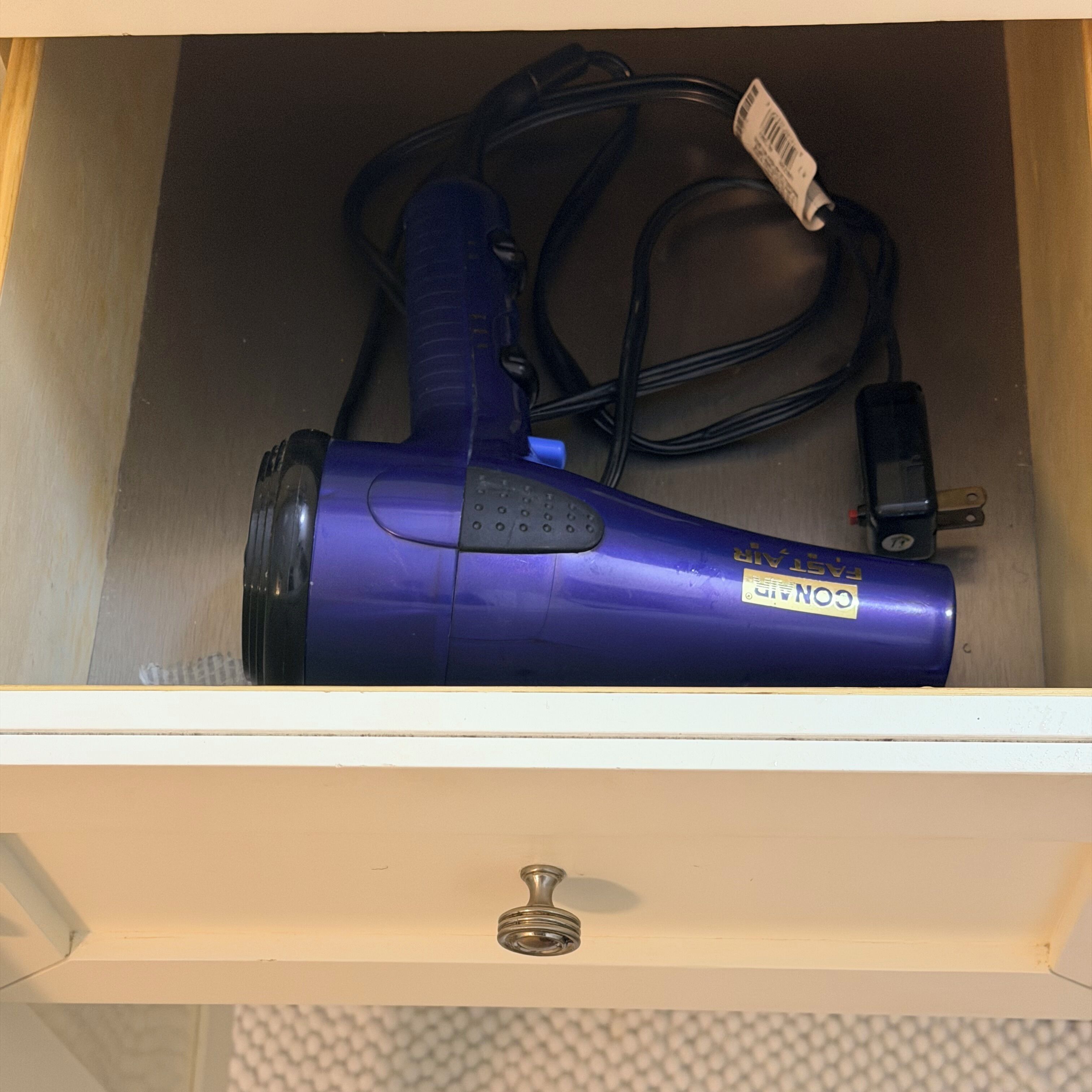 A drawer containing a blue hairdryer with a tag, a power cord, and a remote control.