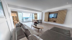 A modern living room with a large sofa, a dining table, and a TV mounted on the wall. - Wave 2 Promenada Apartments (Mamaia-Sat)