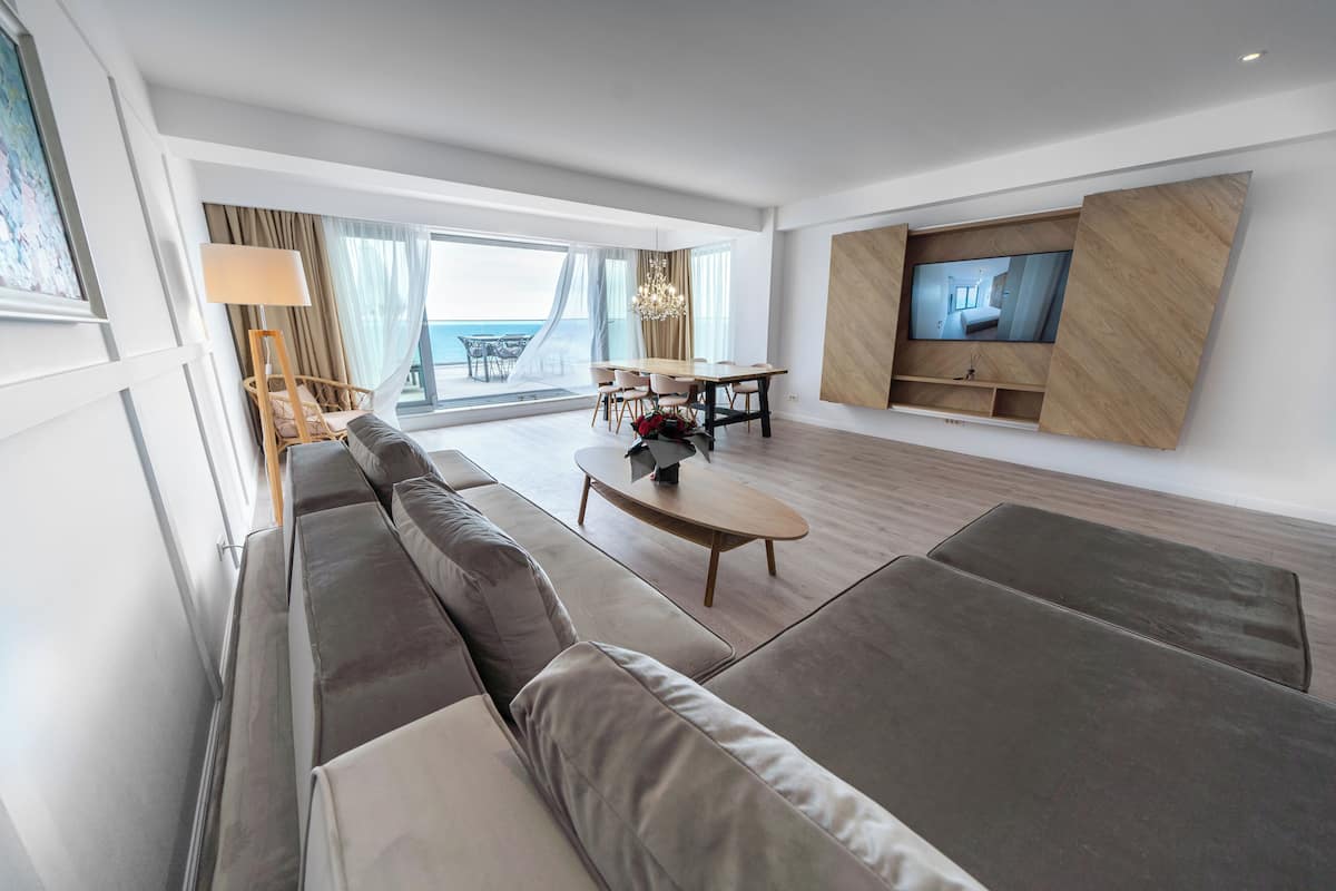 A modern living room with a large sofa, a dining table, and a TV mounted on the wall.