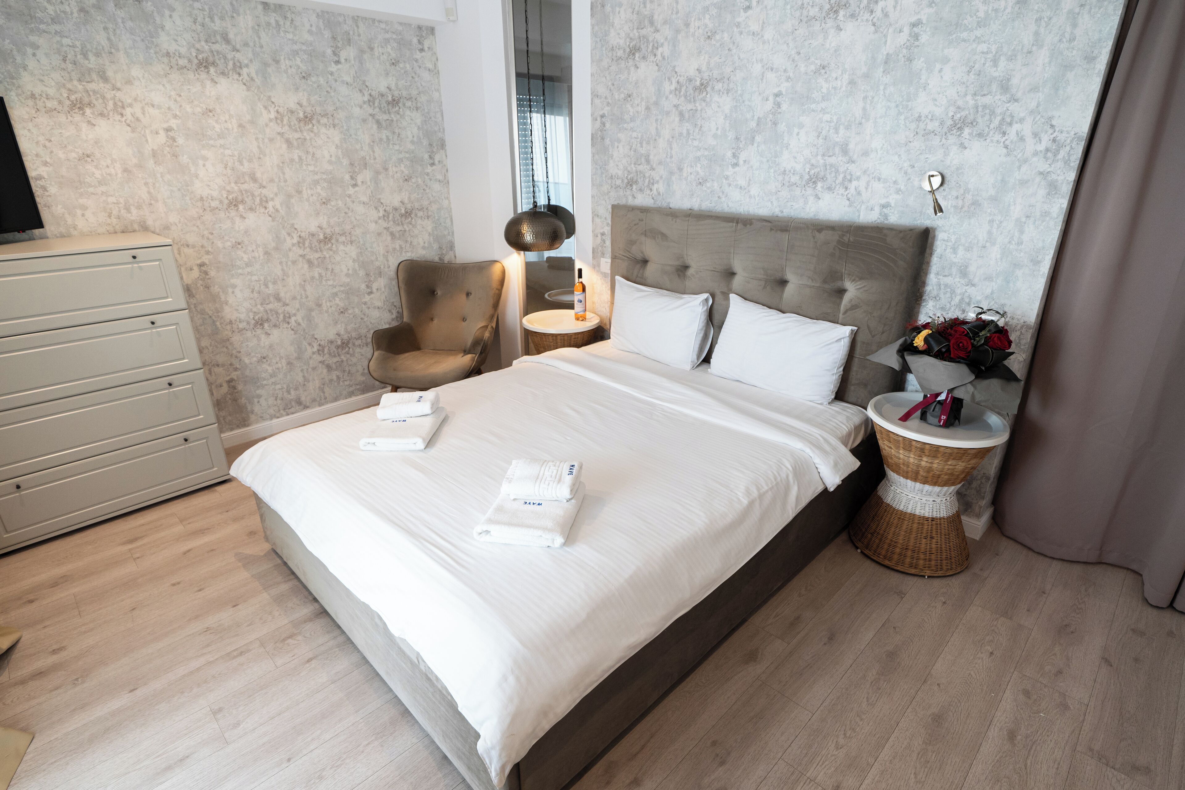 Un lit bien fait, avec du linge de lit blanc, une tête de lit en bois et une table de chevet sur laquelle se trouvent une lampe et une bouteille.