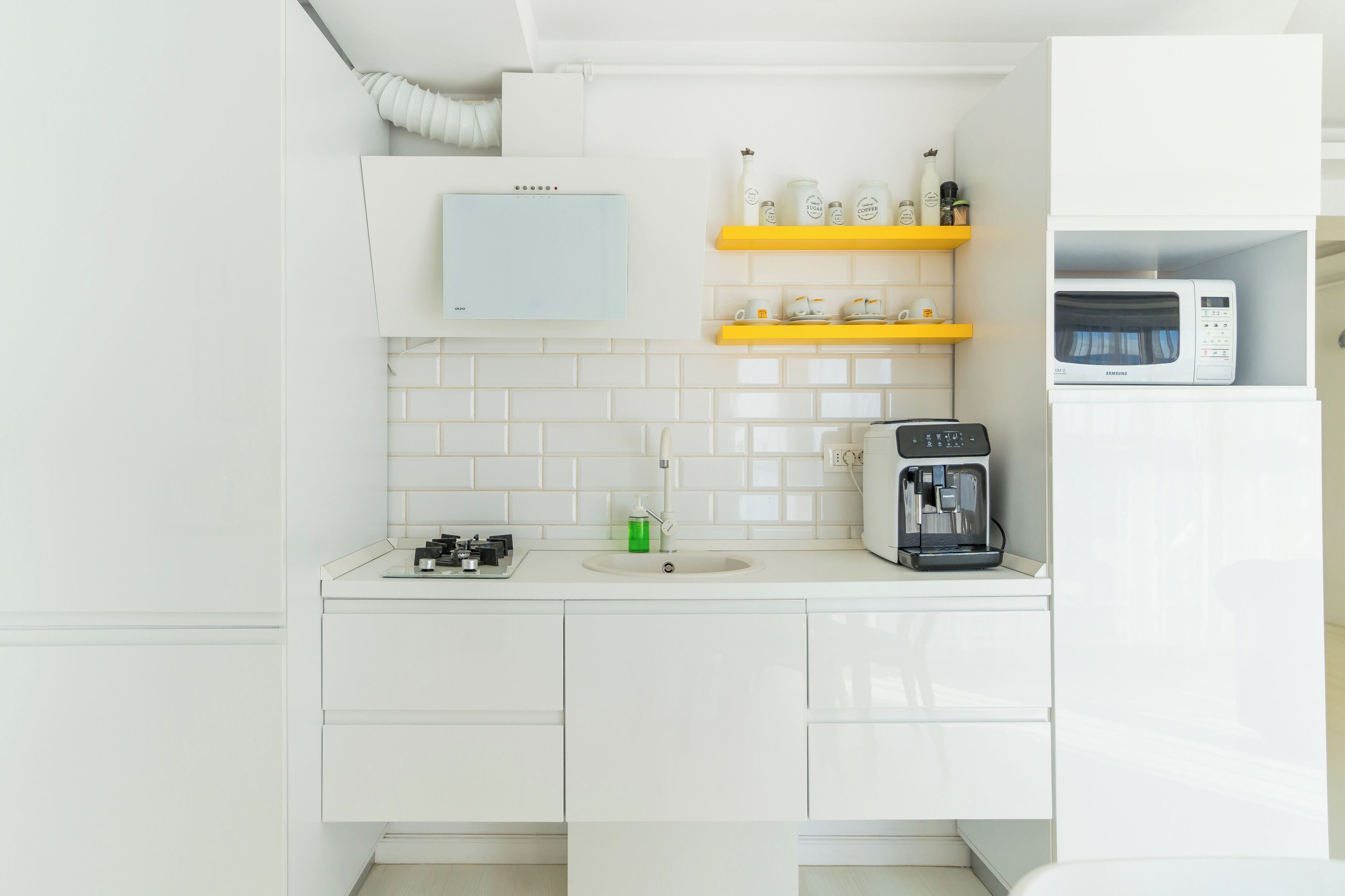 A modern kitchen with white cabinets, a coffee maker, and a microwave on a white countertop.