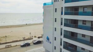 A multi-story building with a visible logo 'WAVE2' on the facade, overlooking a beach with a sandy shore and a calm sea. - Wave 2 Promenada Apartments (Mamaia-Sat)
