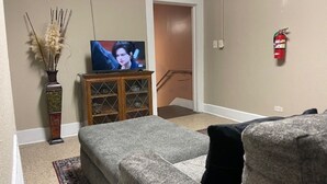 A living room with a television, a vase with dried plants, and a fire extinguisher on the wall. - Downtown Historic home steps away from Festival International (Lafayette)