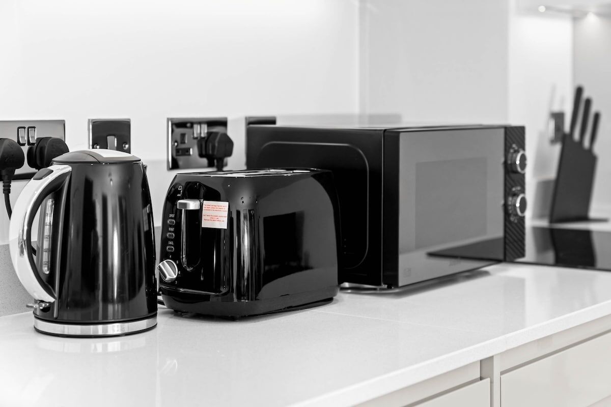 Et køkken med kaffemaskine, brødrister og mikrobølgeovn på en hvid bordplade.