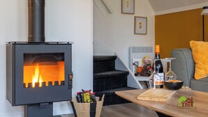 A modern living room with a wood-burning stove, a staircase, a dining area with a table, and a sofa.