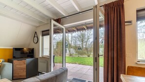 A room with a TV, a sofa, a small table, and a sliding glass door leading to a garden.