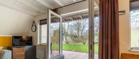 A room with a TV, a sofa, a small table, and a sliding glass door leading to a garden.