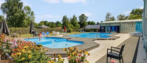 Un área de piscina con múltiples piscinas, sillones de descanso y un espacio de estar cubierto.