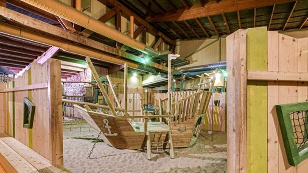 A wooden ship structure with a sandy floor, surrounded by wooden walls and beams, indicating a maritime-themed setting.