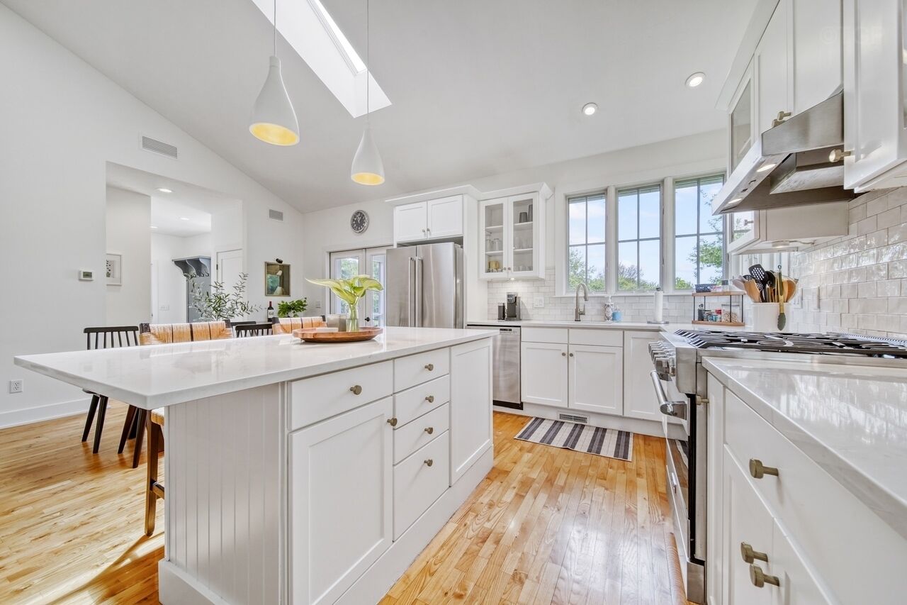 A modern kitchen with white cabinetry, a central island, and a large window providing natural light.