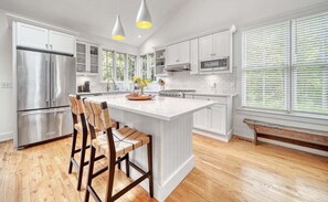 A modern kitchen with white cabinetry, a large island, bar stools, stainless steel appliances, and pendant lighting. - Experience tranquility at The Red Farmhouse in secluded Fennville, MI, with 4 bedrooms. (Fennville)