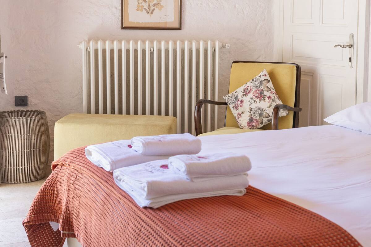 Ein Schlafzimmer mit einem Bett, einem Sessel, einer Heizung und einem gerahmten Bild an der Wand.