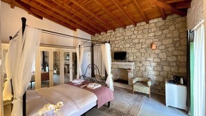 A bedroom with a stone wall, a bed with a canopy, a fireplace, and a television. - La Grenadine Hotel (Cesme)