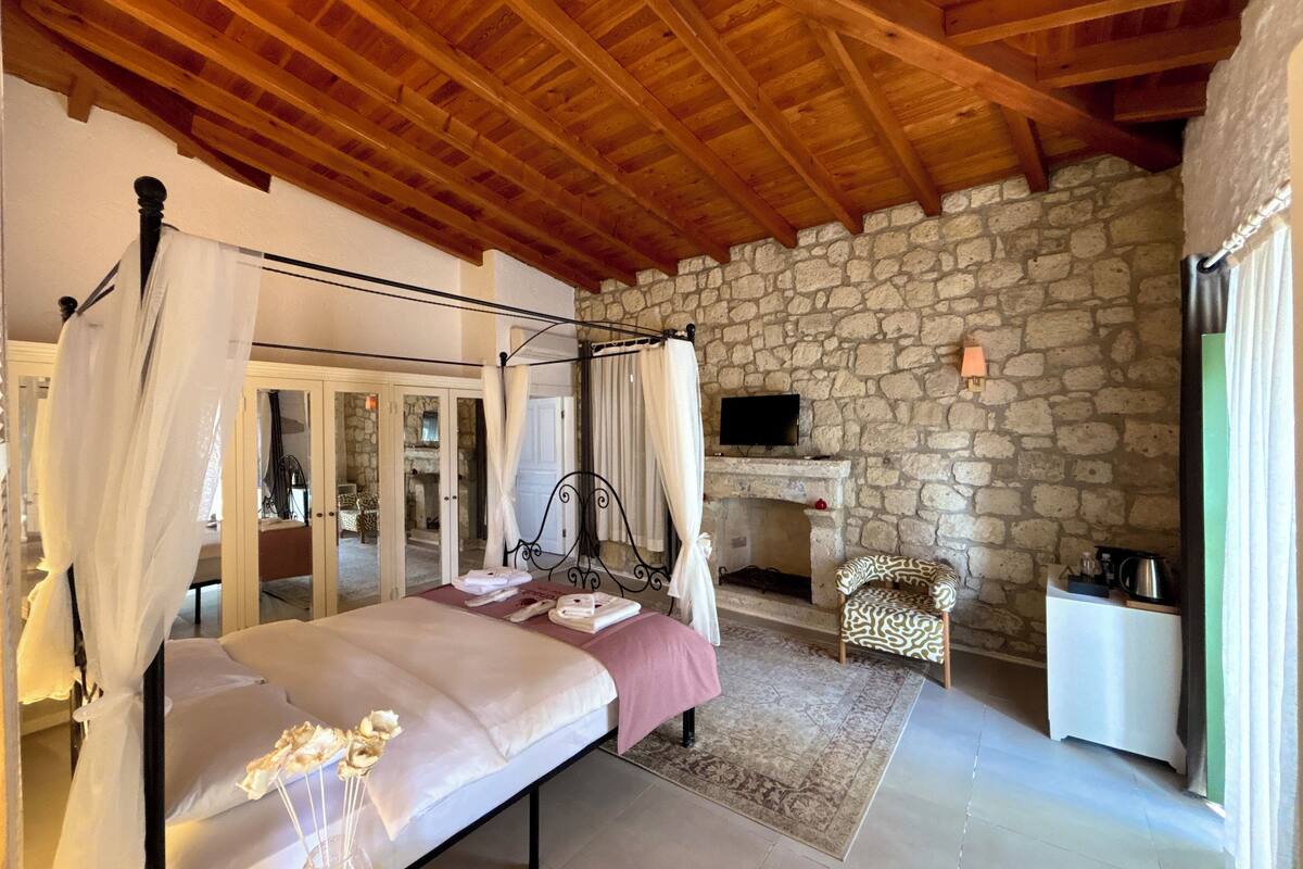Ein Schlafzimmer mit Steinwand, einem Himmelbett, einem Kamin und einem Fernseher.