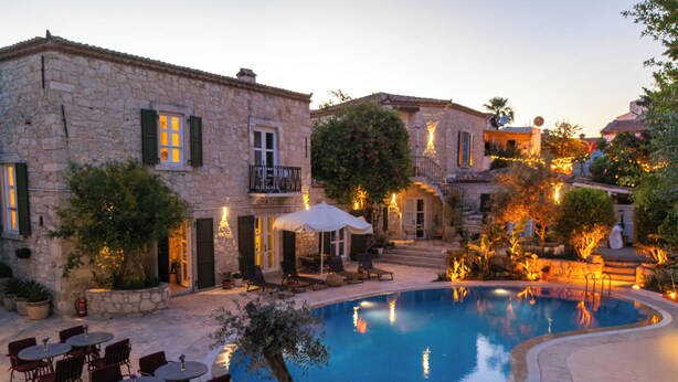 A stone building with a pool, outdoor seating, and a staircase leading to a balcony. - La Grenadine Hotel (Cesme)