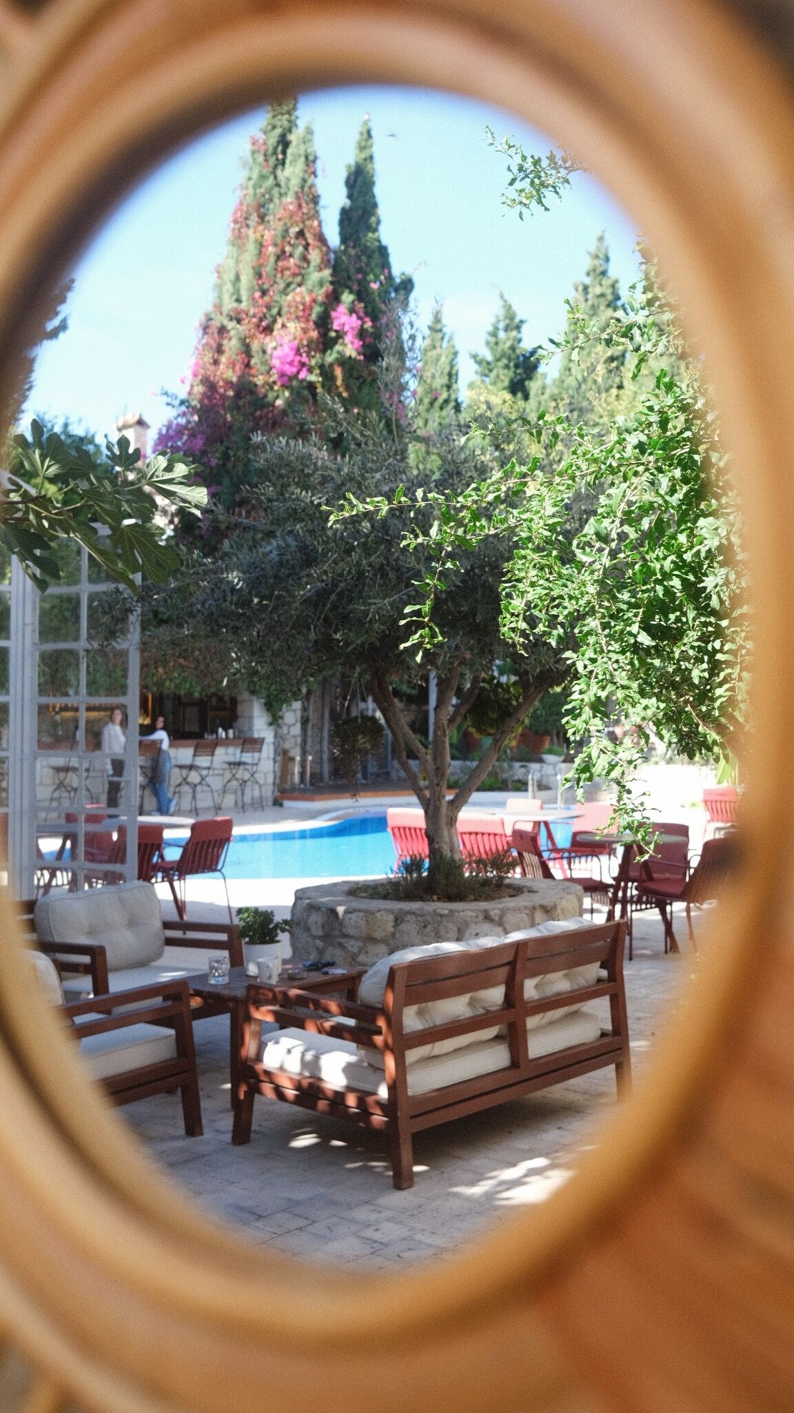 Zona junto a la piscina con bancos y sillas de madera, un muro de piedra y vistas a la piscina y árboles.