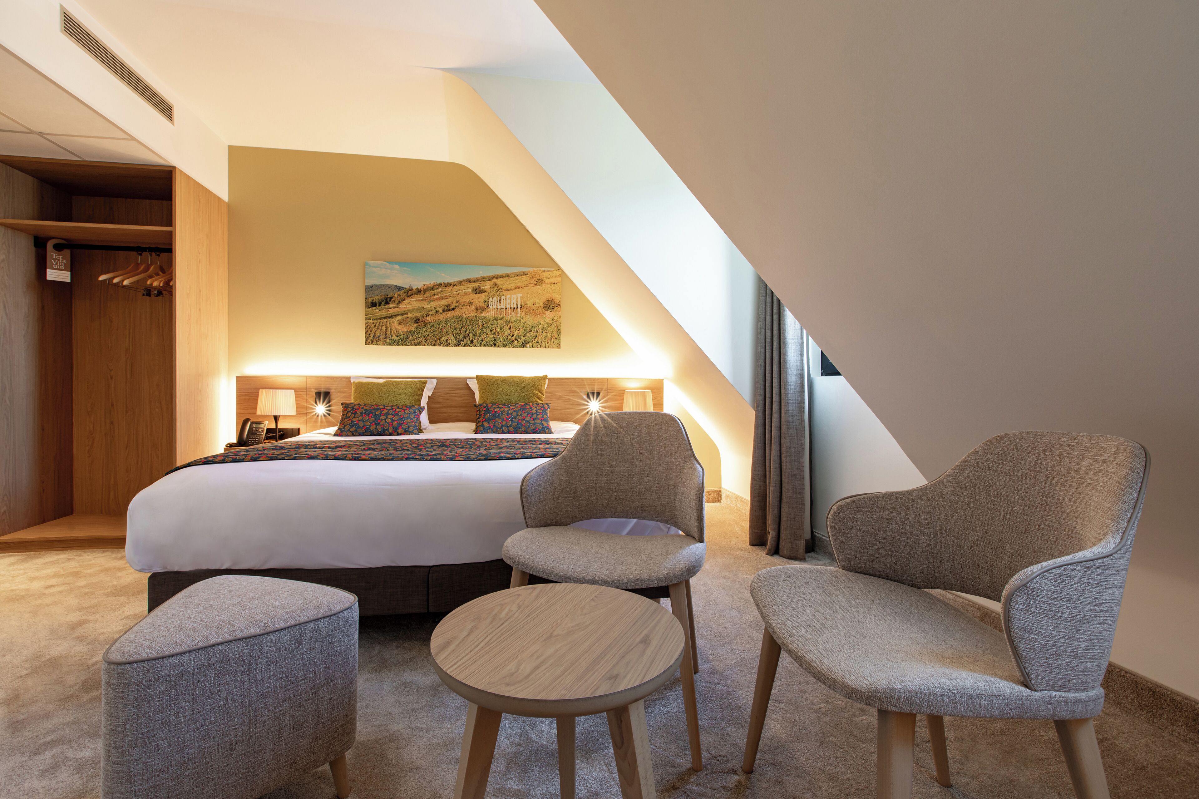 Ett hotellrum med en stor säng, två fåtöljer, ett litet runt bord och en tavla med ett landskapsmotiv på väggen.