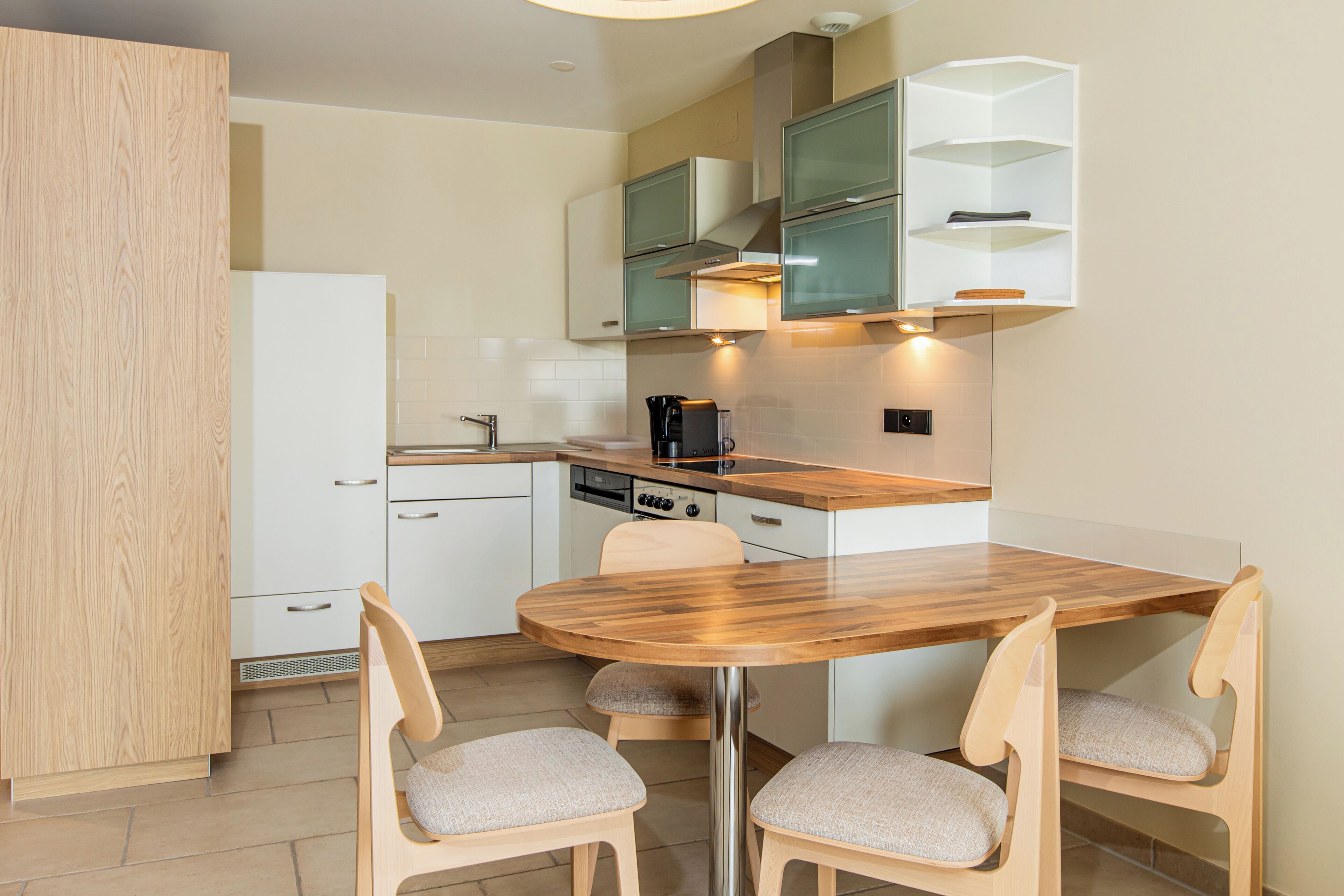 A modern kitchen with a wooden table and chairs, white cabinets, and a built-in oven.