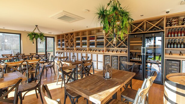 Un ristorante con tavoli e sedie in legno, una credenza per vini e piante pensili.