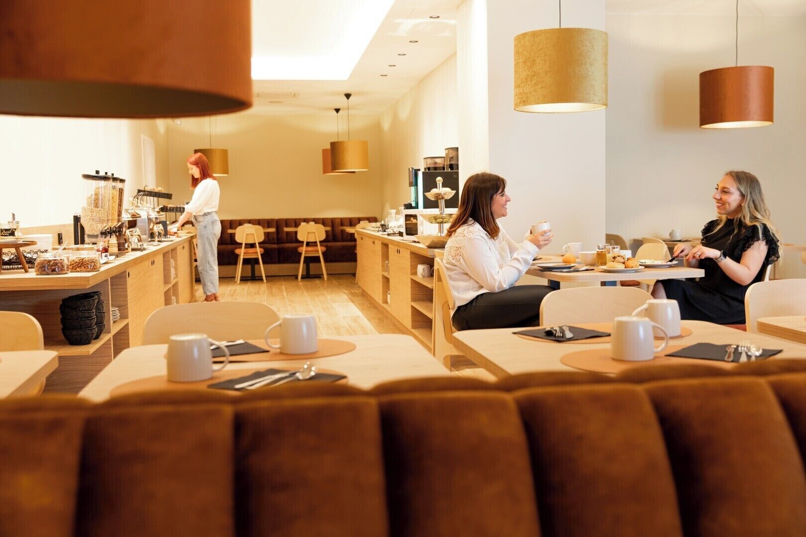 A modern cafe with wooden furniture and pendant lighting.