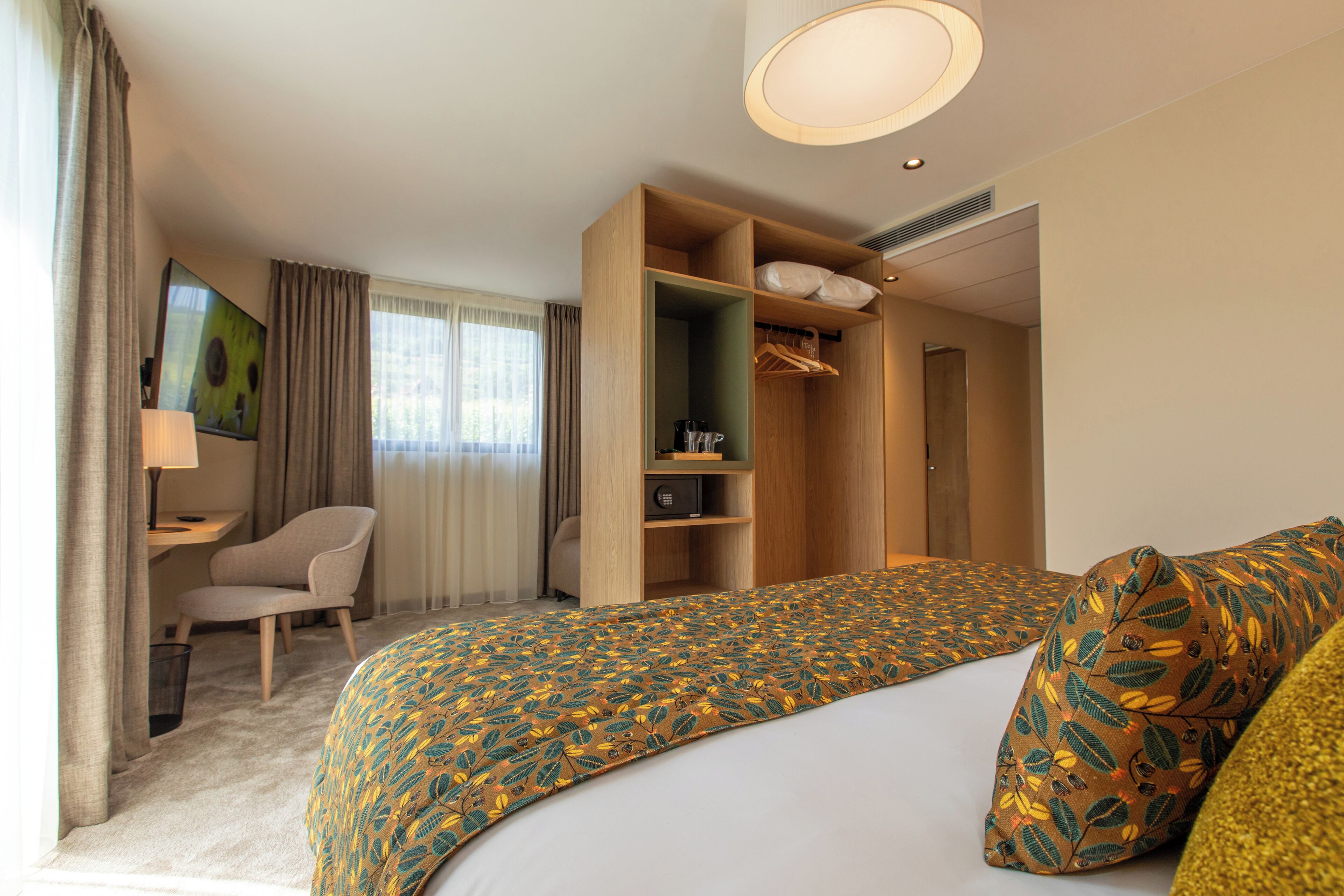 A hotel room with a bed, a desk, a chair, a wardrobe, and a painting on the wall.