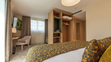 A hotel room with a bed, a desk, a chair, a wardrobe, and a painting on the wall.