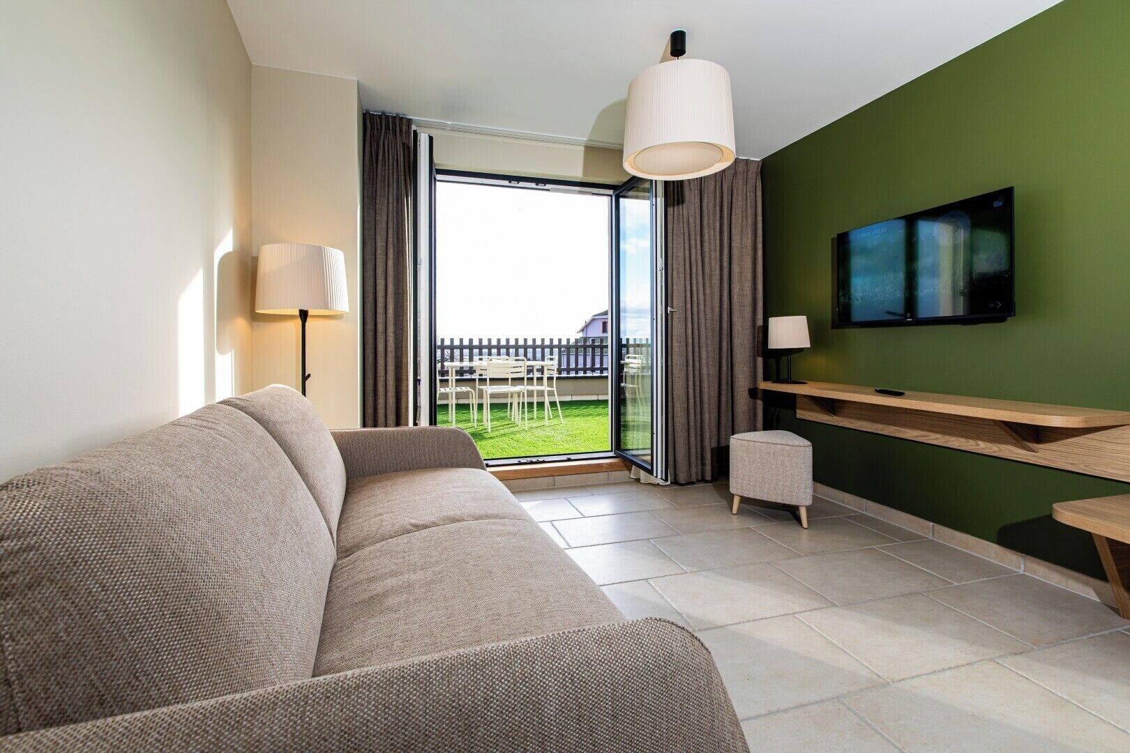 A modern living room with a sofa, a TV, a dining table, and a sliding glass door leading to a balcony.